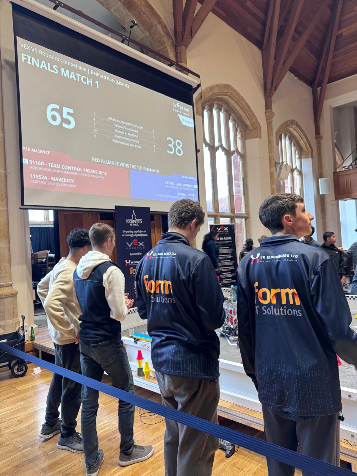 Students wearing Form IT Solutions jackets watching the VEX Robotics final at Bedford School